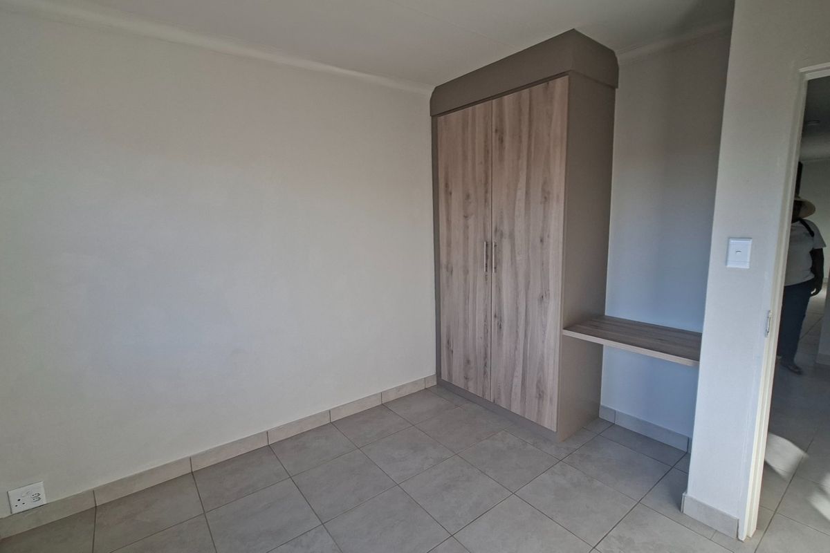A clean, empty bedroom featuring modern tiled flooring and a built-in wardrobe with an integrated desk space.