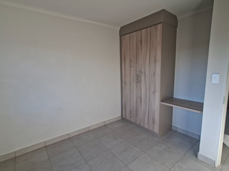 A clean, empty bedroom featuring modern tiled flooring and a built-in wardrobe with an integrated desk space.