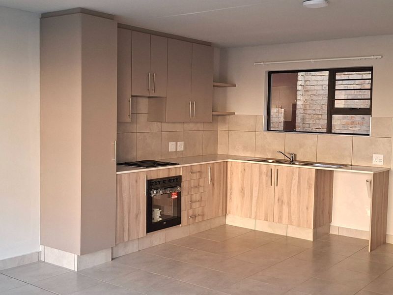 Modern kitchen featuring light wood-tone cabinetry, built-in oven, electric hob, tiled backsplash, and neutral floor tiles in an open-plan layout.