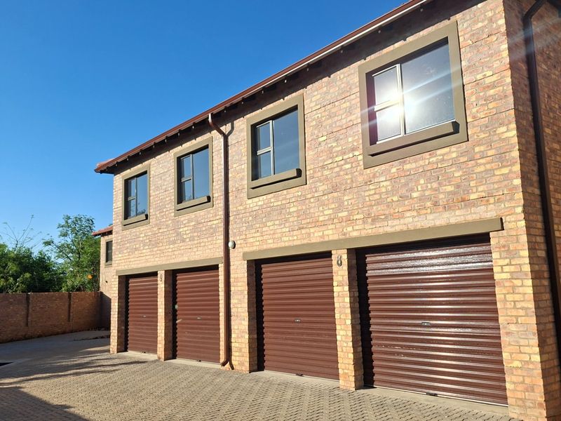 Exterior view of a double-storey townhouse complex featuring face brick construction, multiple roller shutter garage doors, and a paved driveway.