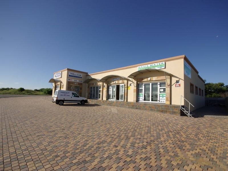 Commercial property exterior featuring a paved parking area, stone-clad facade, and multiple storefront entrances with security gates and awnings.