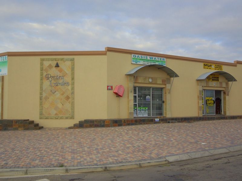 Front exterior view of a commercial retail strip center featuring multiple storefronts with security gates, stone accents, and paved parking area.