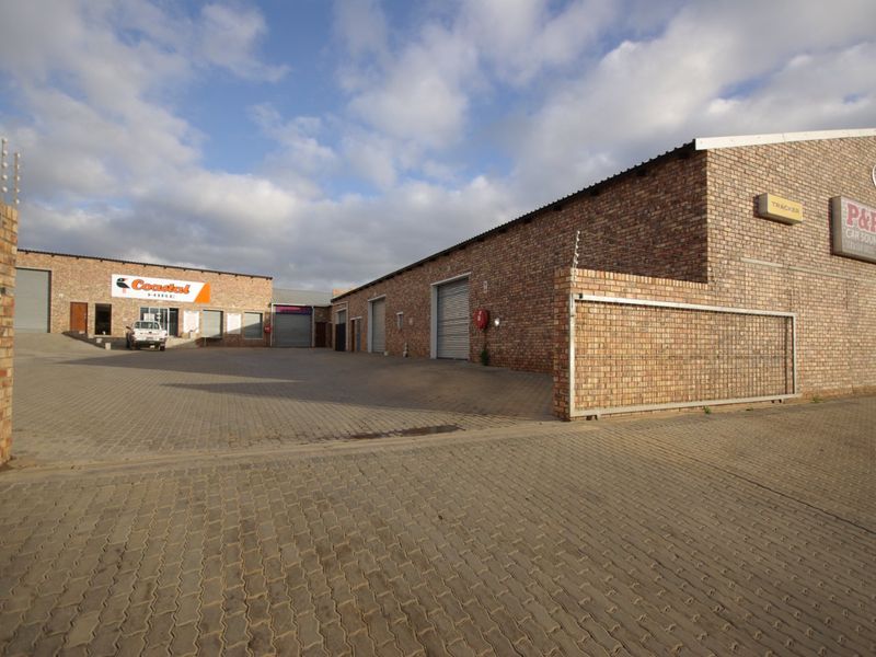 Commercial property exterior featuring face brick construction, multiple roller shutter doors, and a paved yard area with secure perimeter fencing.