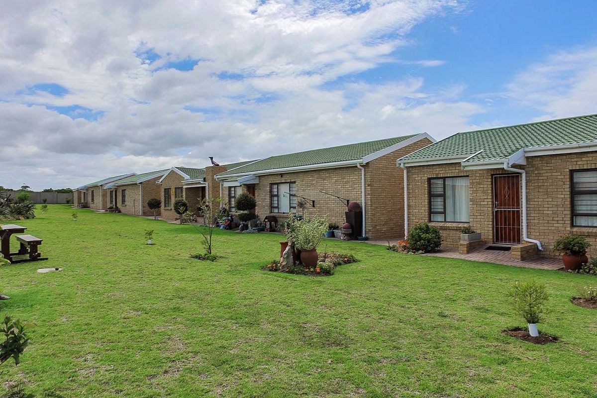 A row of face brick residential units featuring green metal roofs, paved patio areas, and a well-maintained communal lawn.