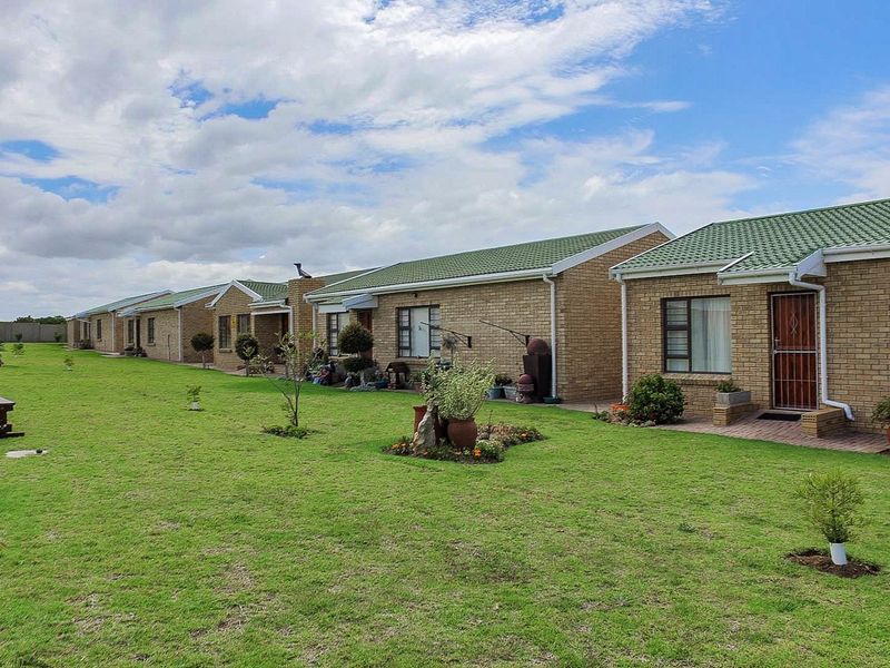 A row of face brick residential units featuring green metal roofs, paved patio areas, and a well-maintained communal lawn.