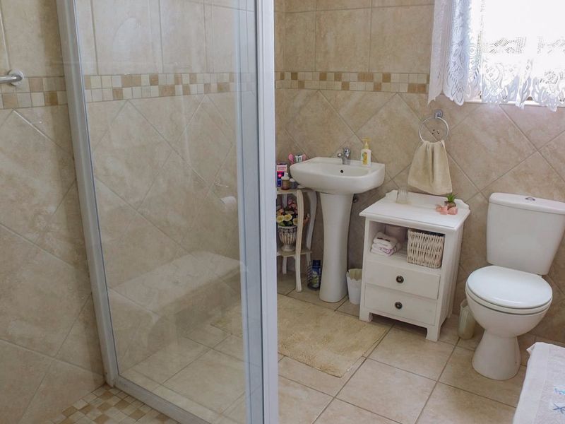 A functional bathroom featuring a pedestal basin, toilet, and a glass-enclosed shower with neutral wall and floor tiling.