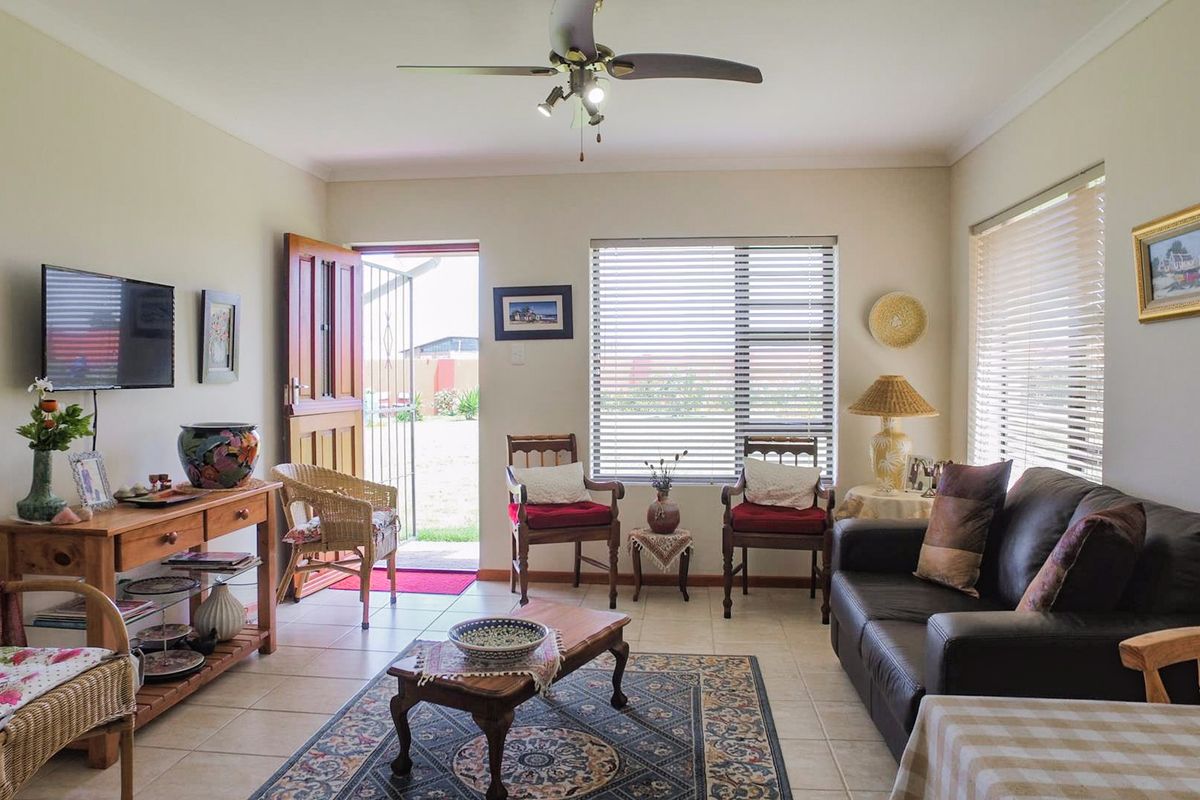 A comfortable living room featuring tiled flooring, a ceiling fan, and natural light through venetian blinds, with direct access to the exterior.