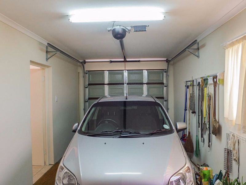 A clean and well-maintained single garage featuring an automatic sectional door, fluorescent lighting, and convenient wall-mounted storage space.