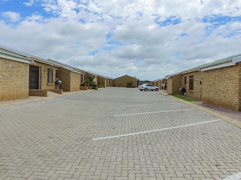 A view of a residential complex featuring face brick units with a shared paved driveway and designated parking bays.