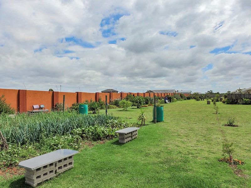 A spacious, well-maintained garden featuring a large lawn area, established vegetable patches, and a secure perimeter wall with electric fencing.