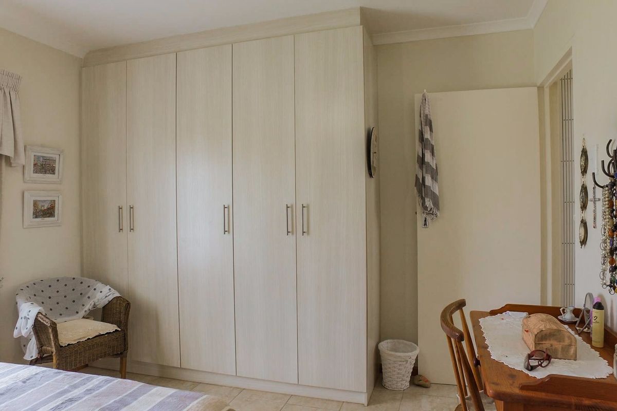 A well-maintained bedroom featuring floor-to-ceiling built-in cupboards with light wood-grain finish and neutral tiled flooring.