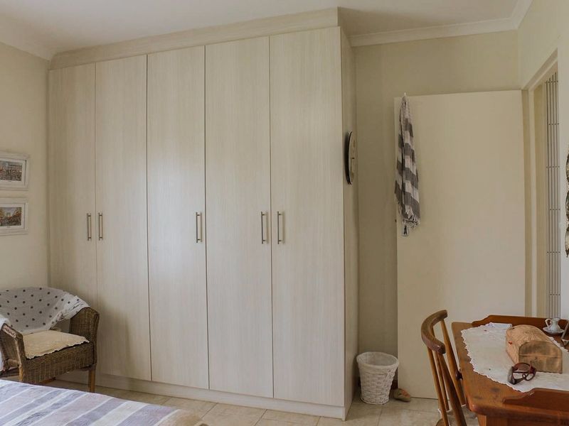 A well-maintained bedroom featuring floor-to-ceiling built-in cupboards with light wood-grain finish and neutral tiled flooring.