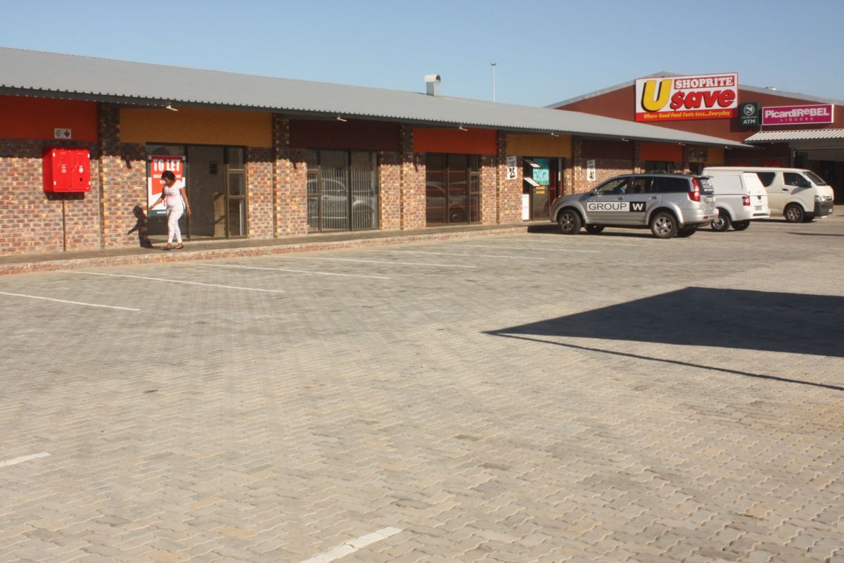 Front exterior view of a commercial retail strip center featuring face brick facade, aluminium shopfronts, and a paved parking area.