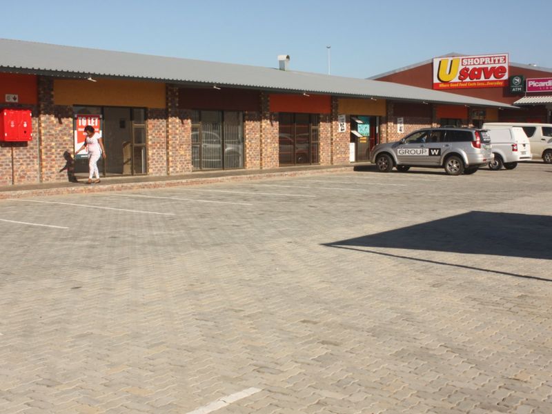 Front exterior view of a commercial retail strip center featuring face brick facade, aluminium shopfronts, and a paved parking area.
