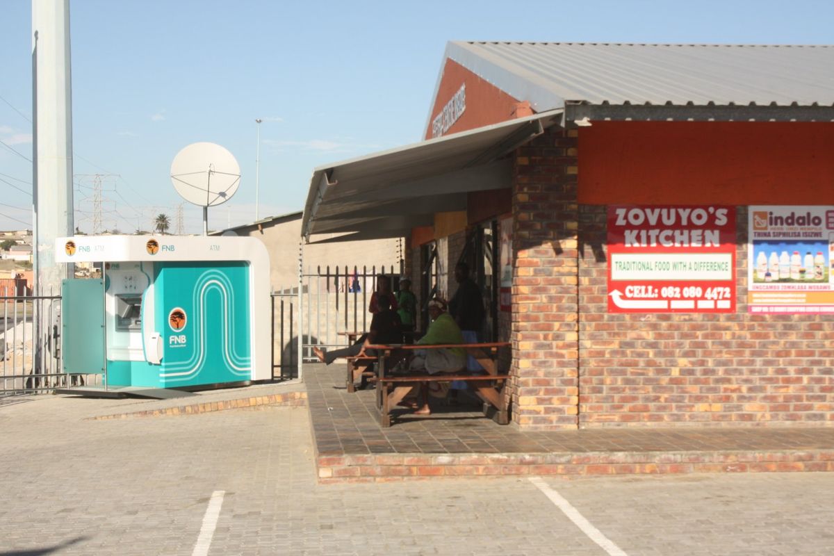 Commercial storefront featuring a brick facade, covered patio area, and an adjacent standalone ATM kiosk in a paved parking setting.
