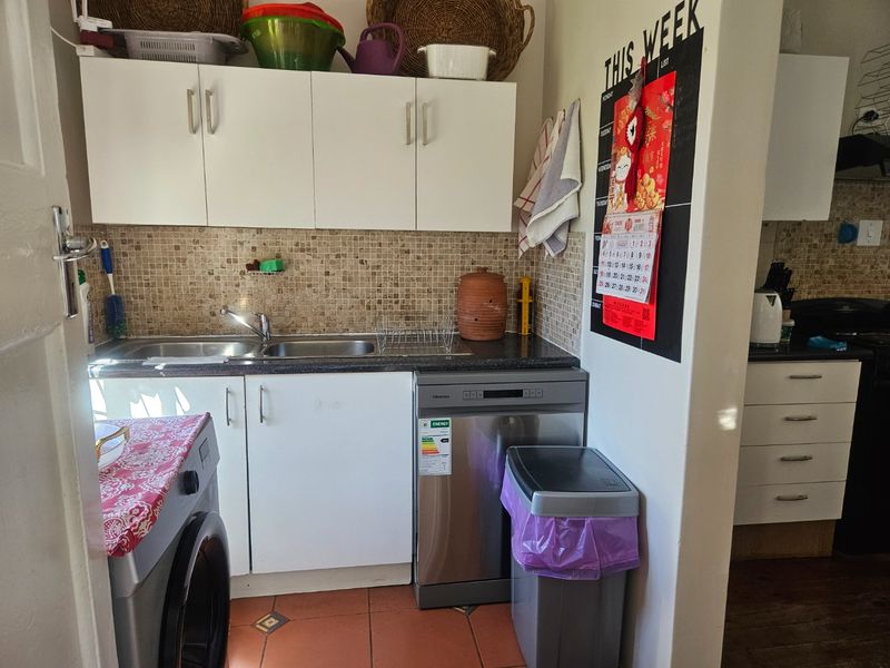 A functional scullery area featuring a stainless steel double sink, tiled backsplash, and ample built-in cabinetry for storage and utility needs.
