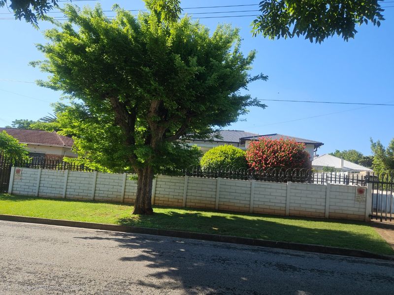 Street view of the property featuring a well-maintained precast concrete boundary wall with security spikes and a mature tree in the front garden.