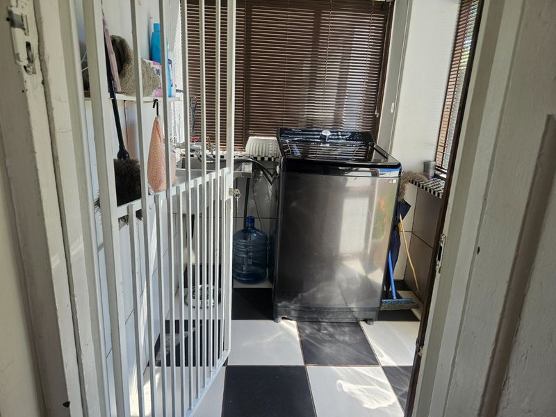 A functional laundry area featuring tiled flooring, a built-in sink, and a security gate, providing a practical space for utility tasks.