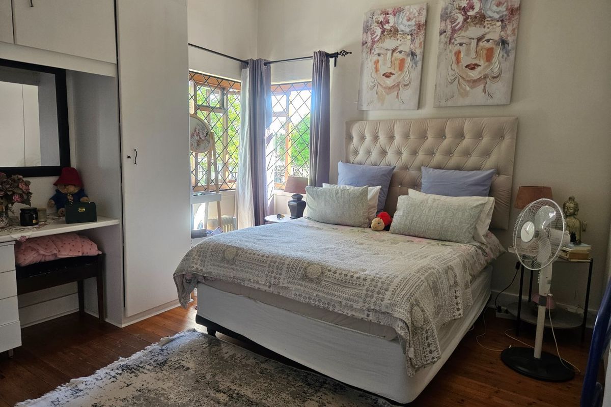 A bedroom featuring timber flooring, built-in wardrobe storage, and windows fitted with security bars, offering a functional and well-lit living space.