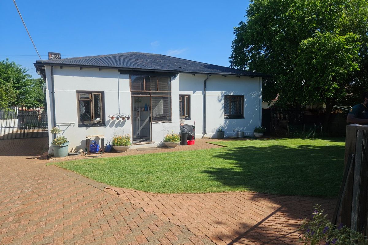 Rear view of the house featuring a paved driveway, well-maintained lawn, and traditional timber-framed windows under a corrugated metal roof.