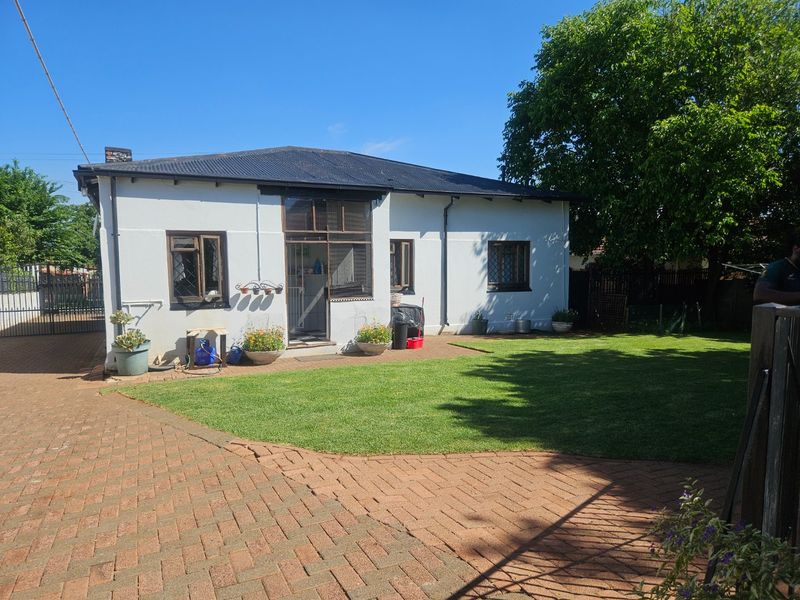 Rear view of the house featuring a paved driveway, well-maintained lawn, and traditional timber-framed windows under a corrugated metal roof.