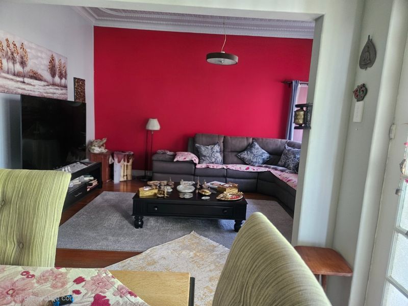 A living room featuring hardwood flooring, decorative ceiling cornicing, and a bold red accent wall, viewed from an adjacent dining area.