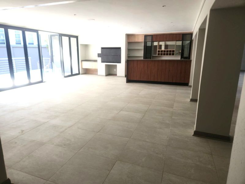 Spacious open-plan living area featuring a built-in bar, integrated braai, large format floor tiles, and expansive stacking doors leading to the outdoor space.