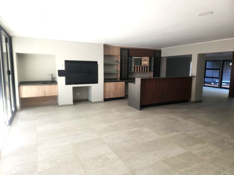 Spacious open-plan living area featuring a modern built-in bar and integrated braai, finished with neutral floor tiles and contemporary cabinetry.