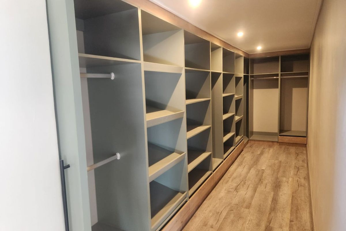 A spacious walk-in closet featuring extensive custom built-in cabinetry with shelving and hanging rails, complemented by modern laminate flooring and recessed lighting.