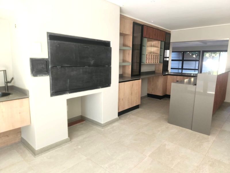 Modern kitchen featuring custom cabinetry, stone countertops, integrated shelving, and a built-in braai, offering a clean and functional space.