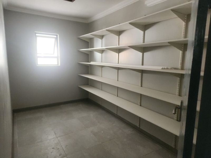 A clean, empty utility or storage room featuring extensive built-in wall shelving, tiled flooring, and a small window for natural light.