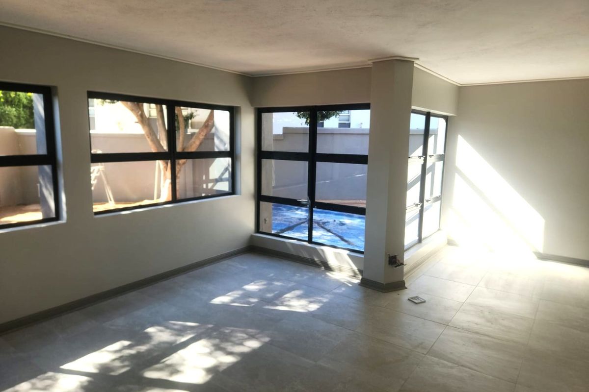 A bright, empty living area featuring large aluminium-framed windows that provide ample natural light and views of the outdoor space.