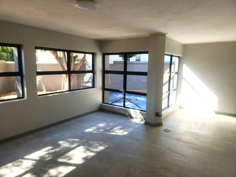 A bright, empty living area featuring large aluminium-framed windows that provide ample natural light and views of the outdoor space.