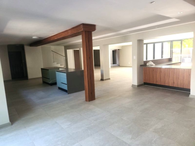 Spacious open-plan living area featuring modern tiled flooring, recessed lighting, and a distinctive timber-slatted column, offering a versatile layout for dining and kitchen integration.