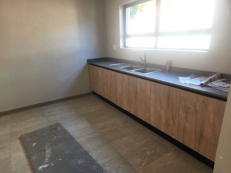 A clean, modern scullery featuring wood-look built-in cabinetry, a double sink with a mixer tap, and neutral tiled flooring.