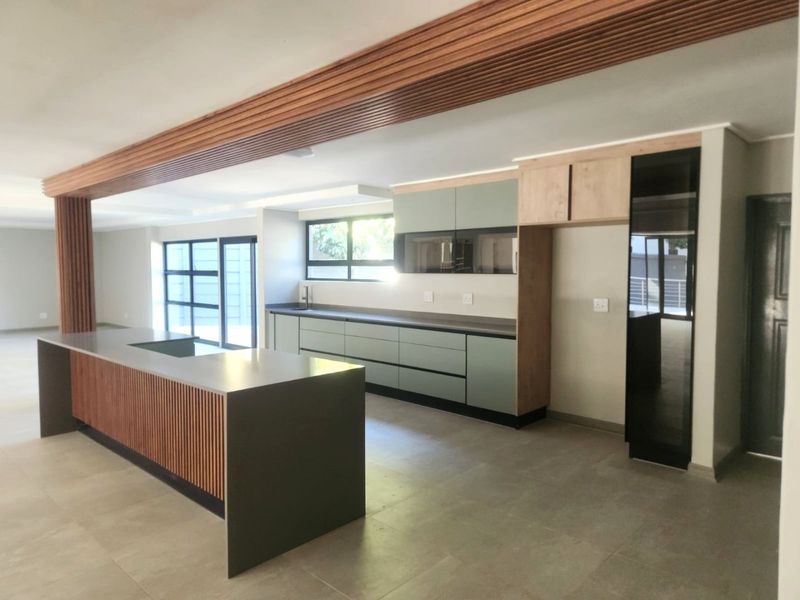 Modern open-plan kitchen featuring a large island with stone countertops, sleek cabinetry, and a distinctive timber slat ceiling detail, flowing into an airy living space.