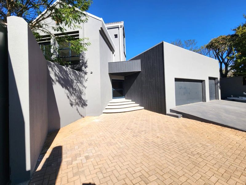 Modern contemporary house exterior featuring a paved driveway, double garage, and a striking stepped entrance with a covered porch area.