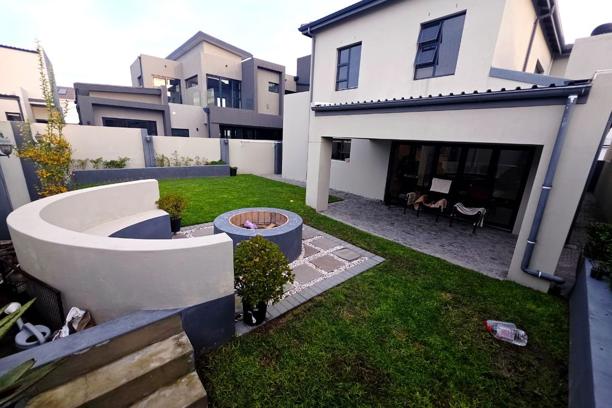 Rear garden featuring a paved patio area, a built-in circular fire pit with a curved concrete bench, and a well-maintained lawn.