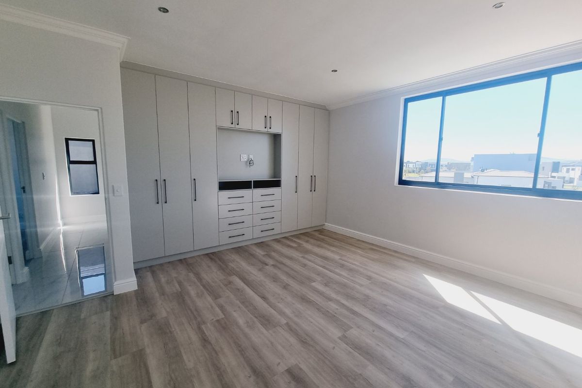 A bright and spacious bedroom featuring modern laminate flooring, extensive built-in cabinetry with integrated storage, and large windows offering natural light.