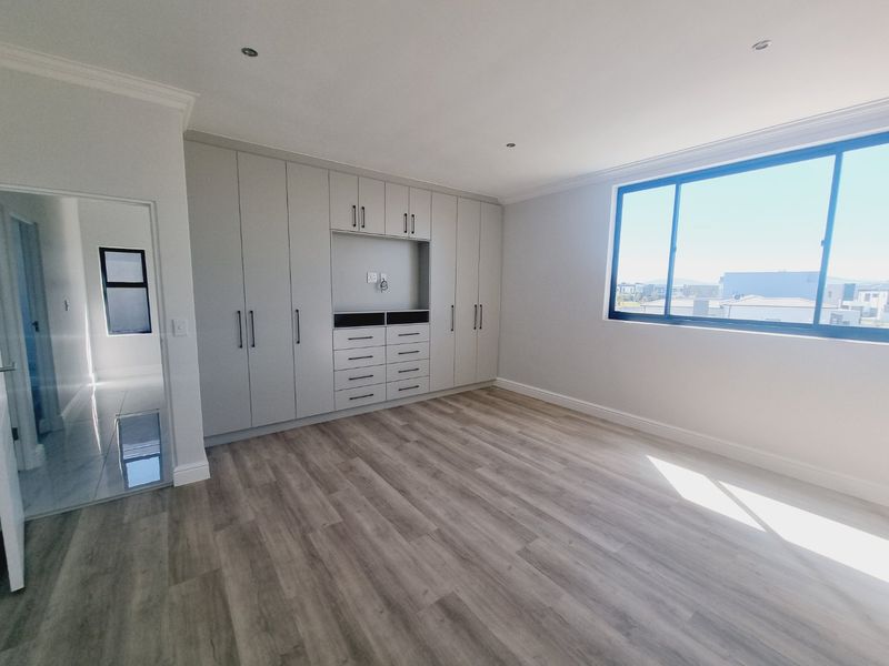 A bright and spacious bedroom featuring modern laminate flooring, extensive built-in cabinetry with integrated storage, and large windows offering natural light.