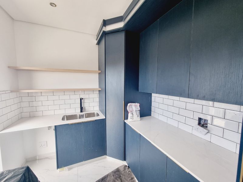 Modern scullery featuring dark blue cabinetry, white quartz countertops, subway tile backsplash, and floating shelves, providing a clean and functional prep area.