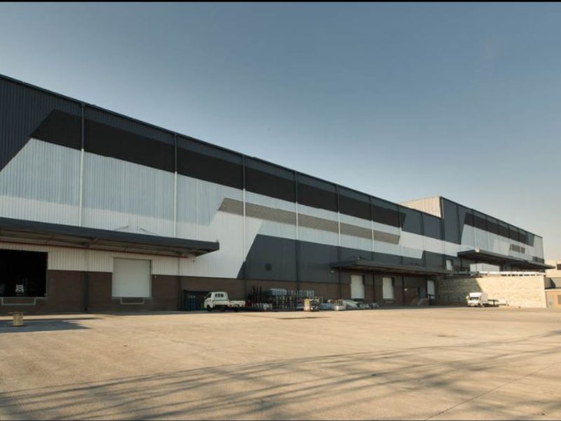 Large industrial warehouse facility featuring extensive concrete yard space, multiple loading bays with roller shutter doors, and modern metal cladding exterior.