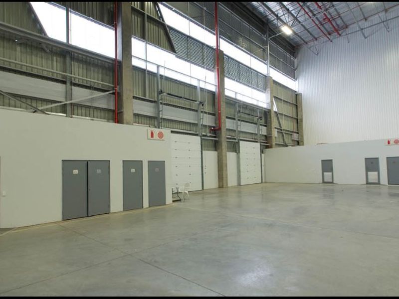 Spacious industrial warehouse unit featuring high ceilings, concrete flooring, integrated fire safety systems, and multiple access points including roller shutter doors.