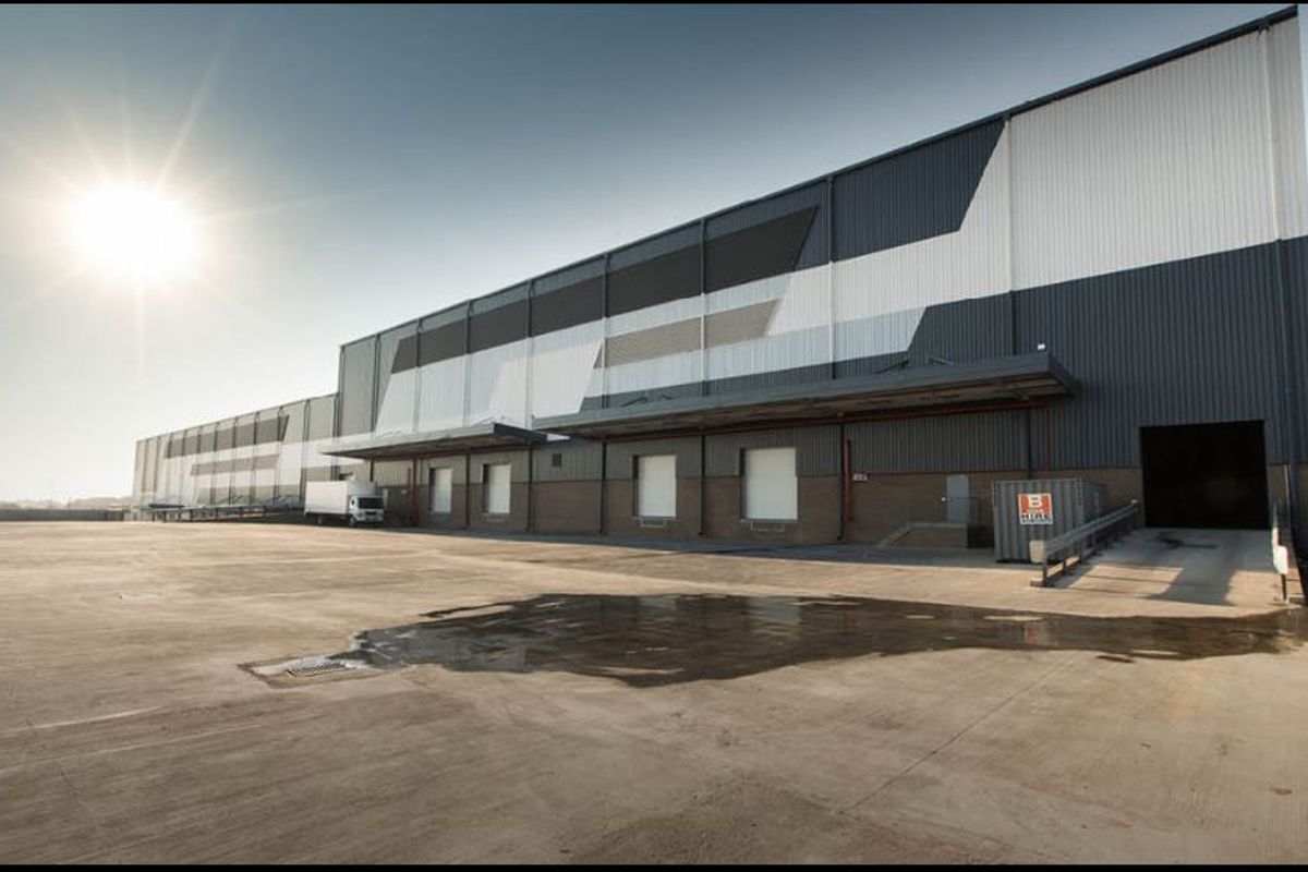 Industrial warehouse exterior featuring a large concrete hardstand, multiple loading docks with canopies, and modern metal cladding.