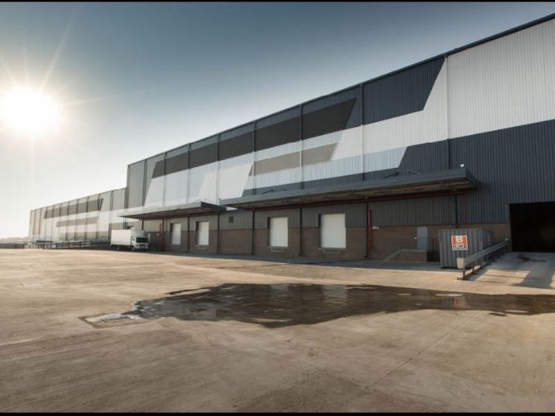 Industrial warehouse exterior featuring a large concrete hardstand, multiple loading docks with canopies, and modern metal cladding.