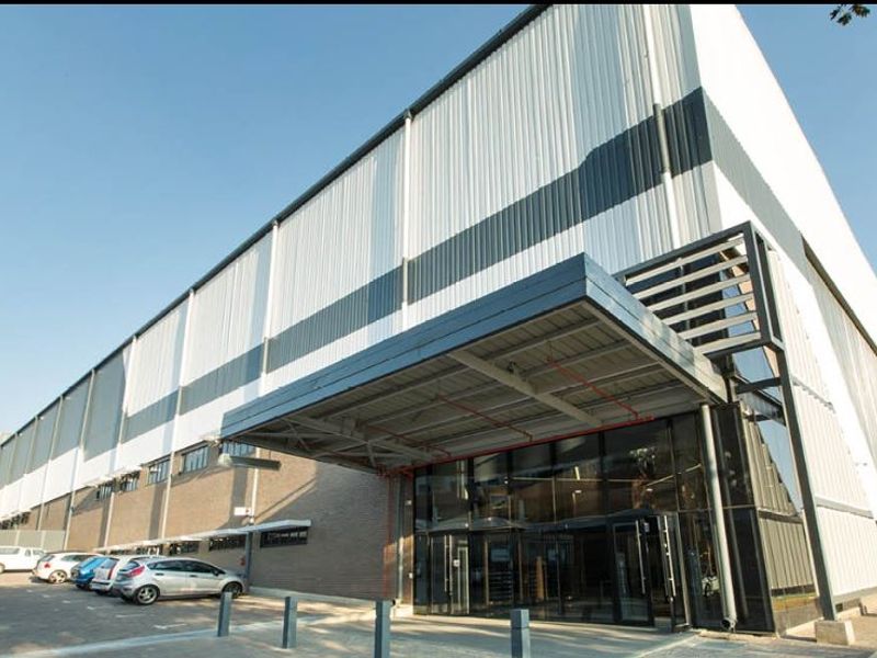 Modern industrial facility featuring a prominent glass entrance, metal cladding, and a covered canopy, providing a professional and well-maintained exterior appearance.