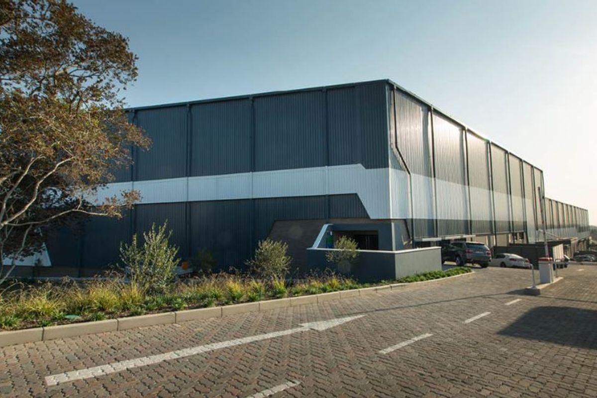 A modern industrial warehouse facility featuring corrugated metal cladding, a paved driveway, and professional landscaping.