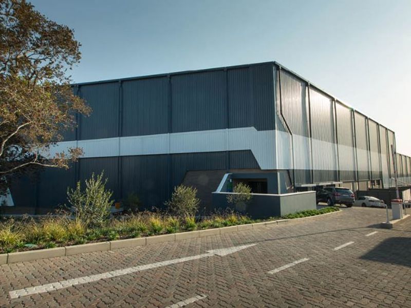 A modern industrial warehouse facility featuring corrugated metal cladding, a paved driveway, and professional landscaping.