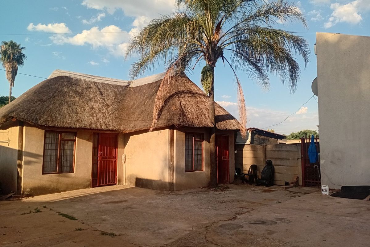 Rear exterior view of a townhouse featuring a traditional thatch roof, concrete paved courtyard, and perimeter boundary walling.