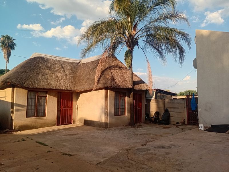 Rear exterior view of a townhouse featuring a traditional thatch roof, concrete paved courtyard, and perimeter boundary walling.